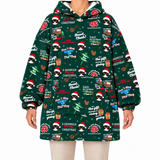 A person wearing a dark green Christmas-themed hooded sweatshirt with an all-over festive print of raccoon faces in Santa hats, holiday quotes, trees, and ornaments, paired with light beige pants against a plain white background.