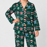 A person wearing a matching long-sleeve pajama set with an all-over Christmas dog print on a dark green background. The pajamas feature cartoon dogs in Santa hats, holiday quotes, musical instruments, and festive graphics.