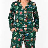 A person wearing a matching long-sleeve pajama set with a dark green Christmas print featuring cartoon dogs in Santa hats, holiday text, and festive illustrations, photographed against a plain light background.