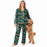 A woman wearing a green Christmas-themed pajama set stands barefoot on a white studio background, holding a fluffy brown dog. The pajamas have an all-over holiday print with Santa, ornaments, reindeer, and festive text.