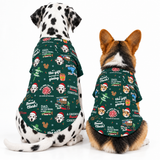Two dogs sitting side by side wearing matching dark green Christmas-themed dog bandanas with a festive print of other dogs, Santa hats, gifts, and holiday text, photographed on a white studio background.