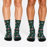 Three pairs of crew socks worn on legs, featuring a dark green background with a colorful 'DAD' themed pattern of cartoon characters, brains, and text like 'DAD TUMOR'.