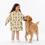 A young girl wearing a long-sleeve hooded pajama shirt with a green cactus and cartoon character print, standing next to a golden retriever dog on a white studio background.