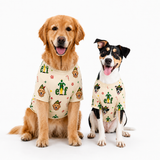 Two dogs wearing matching beige Christmas-themed dog shirts with green elf hats and colorful holiday prints, posed against a clean white background.