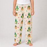 A person wearing cream-colored fleece pajama pants with a festive elf print, standing against a light gray studio background.
