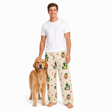 A man wearing a white t-shirt and Christmas elf-print pajama pants stands next to a golden retriever dog on a solid white background.