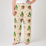 A person wearing cream-colored lounge pants with a repeating print of green elf figures, corgi dog faces, candy canes, and paw prints, shown against a light gray studio background.