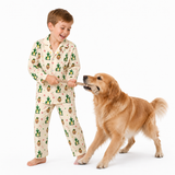 A young boy wearing cream-colored pajamas with a green cactus and acorn pattern is playfully pulling a golden retriever dog on a wooden toy against a solid white background.