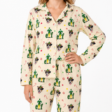 A woman wearing a matching long-sleeve pajama set with a festive Elf the Page pattern, featuring green elf silhouettes, dog faces, and candy canes on a cream background.