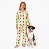 A young girl stands barefoot next to a black and white dog, both wearing matching cream-colored pajamas with a green cactus and small red flower pattern, against a plain white studio background.