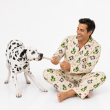 A man wearing beige panda-print pajamas sits cross-legged on a white studio floor, playfully pulling a rope with a black-and-white Dalmatian dog.