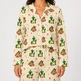 A model wearing a matching long-sleeve pajama set with a festive Christmas Elf print. The pajamas feature a cream-colored base with a repeating pattern of green elf figures, brown dog faces, candy canes, and paw prints.