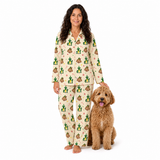 A woman wearing a cream-colored pajama set with a green and brown poop-themed cartoon pattern stands next to a fluffy brown dog on a solid white background.