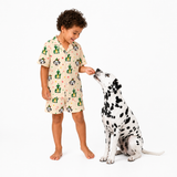 A young child wearing a short-sleeve pajama set with a Dalmatian dog sitting beside them on a plain white studio background. The pajamas are light beige with a cartoon print of cacti and Dalmatians.