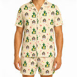 A man wearing a two-piece short-sleeve pajama set with a Christmas elf pattern on a light beige background. The pajama set includes a button-up shirt and matching shorts, featuring green elf figures, Santa hats, candy canes, and dog faces.