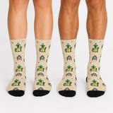 Three pairs of crew socks worn on legs, featuring a repeating pattern of green elf figures, small yellow stars, and cartoon dog faces on a light beige background, with black toes and heels.