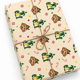 A gift box wrapped in cream-colored Christmas paper featuring a repeating pattern of Buddy the Elf, green elf figures, candy canes, and peppermint candies, tied with natural twine.