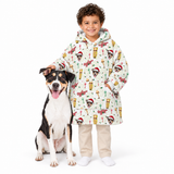 A child wearing a long hooded Christmas-themed coat with a dog print pattern, standing next to a black and white dog on a solid white background.