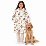 A young girl stands next to a golden retriever dog wearing a long white hooded blanket with a festive Christmas print of dogs in Santa hats, candy canes, and holiday decorations. The girl is also wearing beige pants and white socks, set against a solid white studio background.