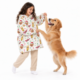 A young girl wearing a white hooded robe with a colorful dog-themed print and beige sweatpants is playfully holding hands with a golden retriever dog against a solid white background.