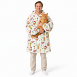 A man wearing a white hooded blanket robe with a festive Christmas print, holding an orange tabby cat against a solid white background.