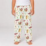 A child wearing cream-colored Christmas-themed pajama pants with a repeating pattern of corgi faces in Santa hats, lighthouses, and the word 'Christmas' in red script, shown against a light gray studio background.