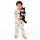 A young boy wearing a festive holiday-themed pajama set with a black and white cat, standing against a solid white studio background.