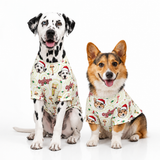 Two dogs, a Dalmatian and a Corgi, sitting side-by-side wearing matching holiday-themed dog shirts with a cream background and festive illustrations.