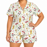 A woman modeling a matching short-sleeve button-front pajama top and shorts set with a festive holiday print featuring Dalmatian faces, cocktail glasses, Christmas hats, and the word 'O'Rear' on a white background.