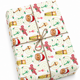 A wrapped gift box with a festive holiday print featuring Santa Claus faces, beer glasses, holly leaves, and the word 'O'Jolly' on a white background, tied with brown string.