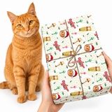 An orange tabby cat sits beside a person holding a wrapped gift box. The gift box is wrapped in white paper with a repeating cat-themed pattern and tied with brown string, on a clean white background.