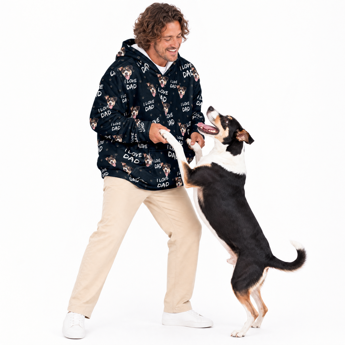 Man wearing a black blanket hoodie with dog patterns, interacting with a dog on a white background