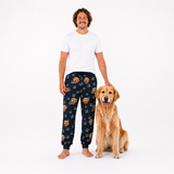 Smiling man in white tee and black dog-print I Love Dad sweatpants standing beside a golden retriever
