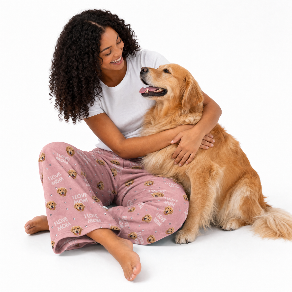 Woman in pink pajama pants with dog pattern sitting on the floor with a golden retriever.