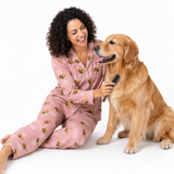Woman in pink pajamas with dog pattern sitting next to a golden retriever on a white background