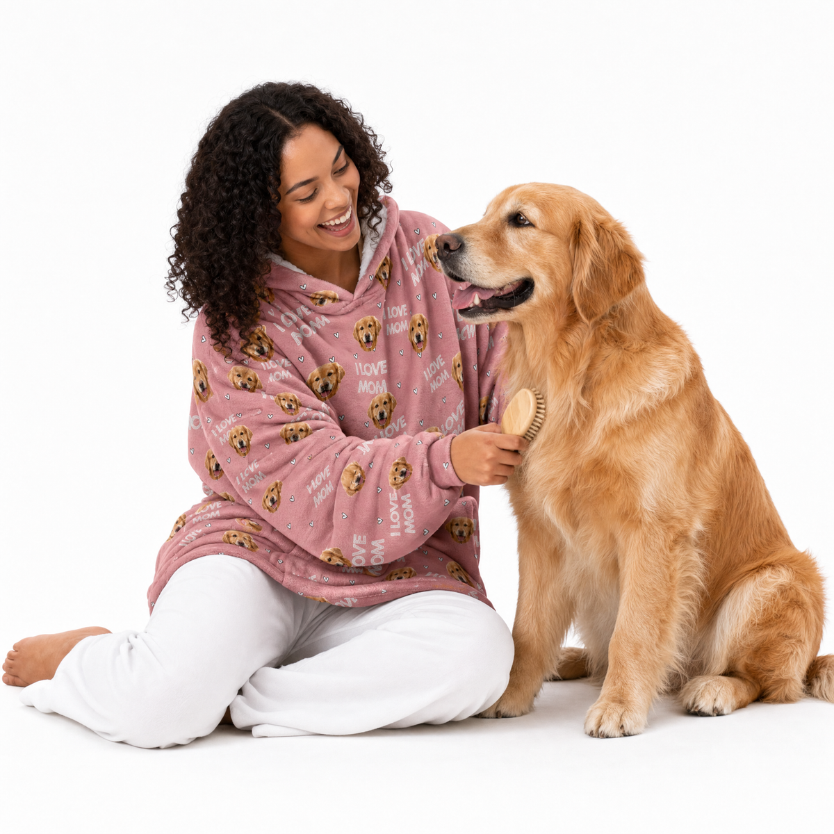 Woman wearing a pink patterned blanket hoodie sitting with a large dog on a white background
