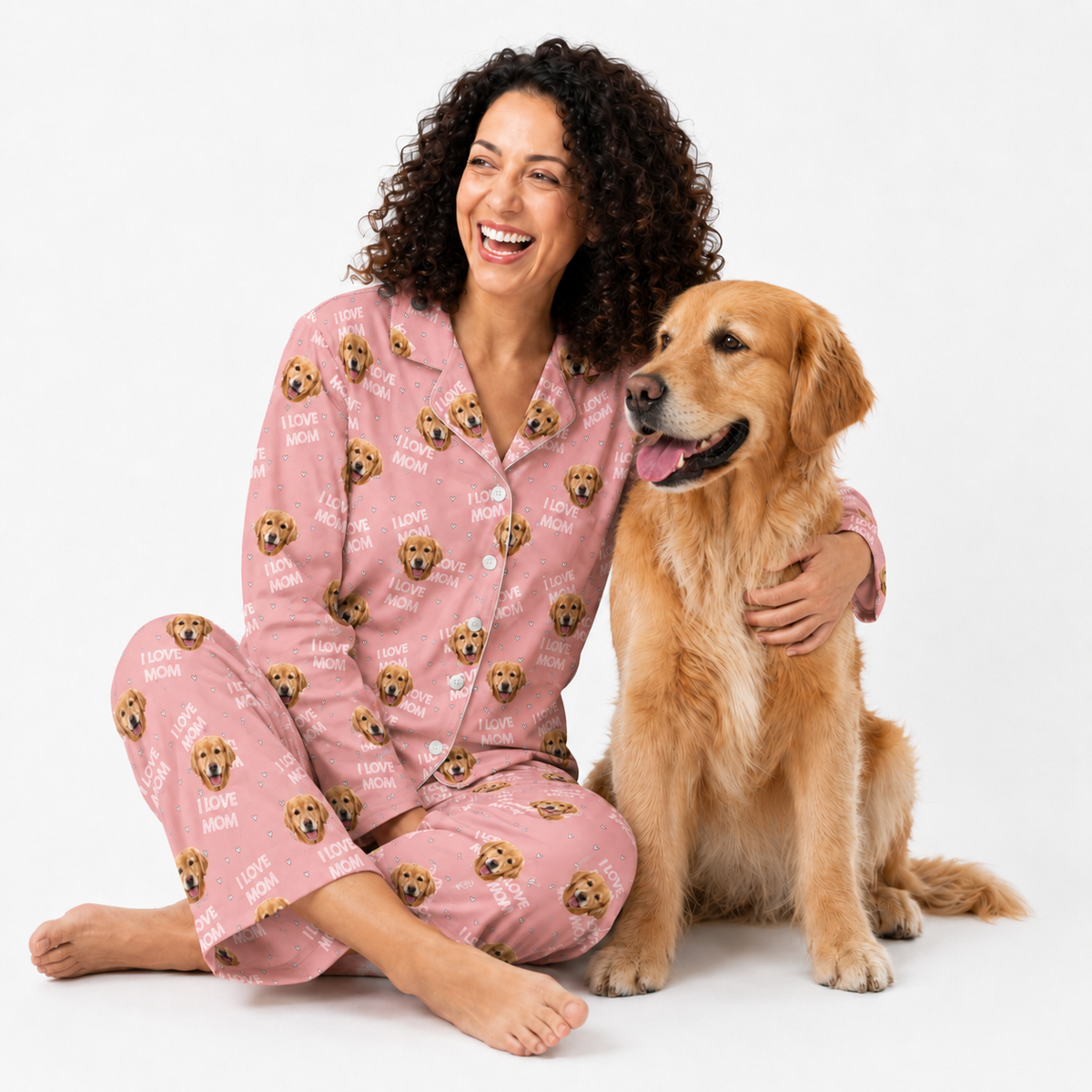 Woman in pink pajamas with dog pattern sitting next to a golden retriever on a white background