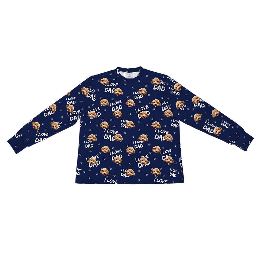 A navy blue long-sleeve pajama top with a crew neck. It features a repeating custom pattern of a light brown Goldendoodle's face, interspersed with the white text "I LOVE DAD" and small white paw prints.