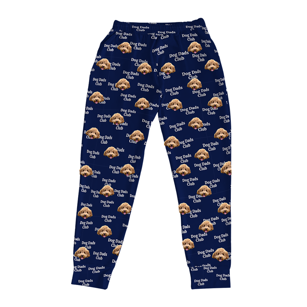 Navy jogger pajama pants with an all-over pattern featuring a brown curly-haired dog’s face, white paw prints, and the repeated phrase ‘I LOVE DAD,’ displayed flat on a white background.