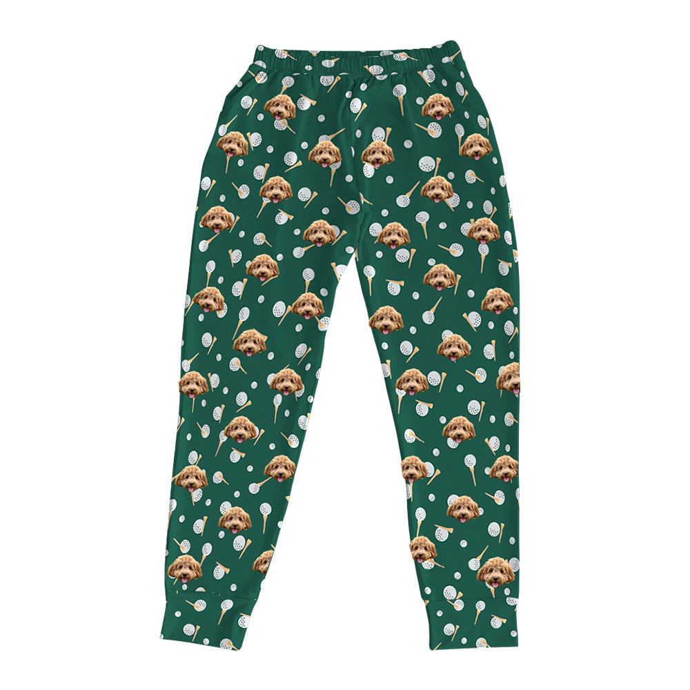 Dark green pajama joggers covered in a repeating golf-themed pattern. The pattern features alternating elements: white golf balls, light yellow golf tees, and smiling headshots of a light brown dog.