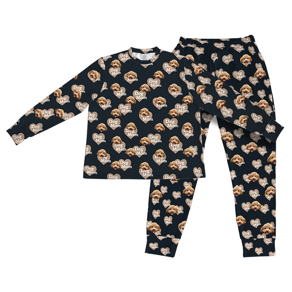 A matching set of long-sleeve pajama top and jogger bottoms, in a black/dark navy fabric. The entire set is covered in a repeating pattern featuring alternating elements: light brown heart shapes with the text "Dog Mom" inside, and smiling headshots of a dog.