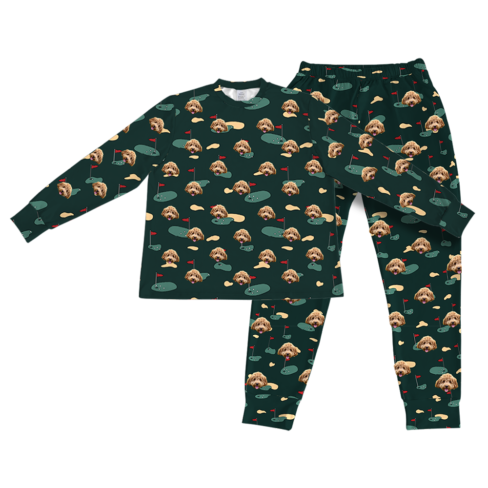 A matching set of long-sleeve pajama top and jogger bottoms, in a dark hunter green fabric. The entire set is covered in a repeating golf-themed pattern featuring alternating elements: cartoon depictions of golf putting greens with a red flag, yellowish sand traps, and smiling headshots of a small brown dog 
