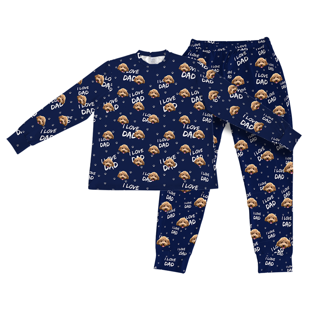 A matching set of long-sleeve pajama top and jogger bottoms, in a dark navy blue fabric. The entire set is covered in a repeating pattern featuring alternating elements: the phrase "I LOVE DAD" in white text, and smiling headshots of a dog.