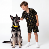Child wearing a batman pajama set standing next to a dog on a white background