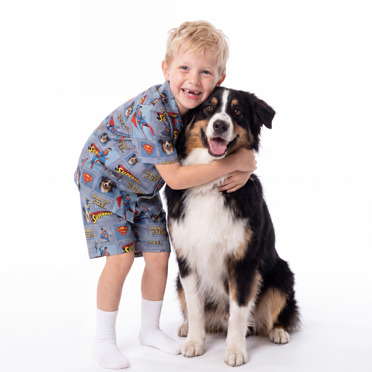Child wearing a superman pajama set hugging a dog on a white background