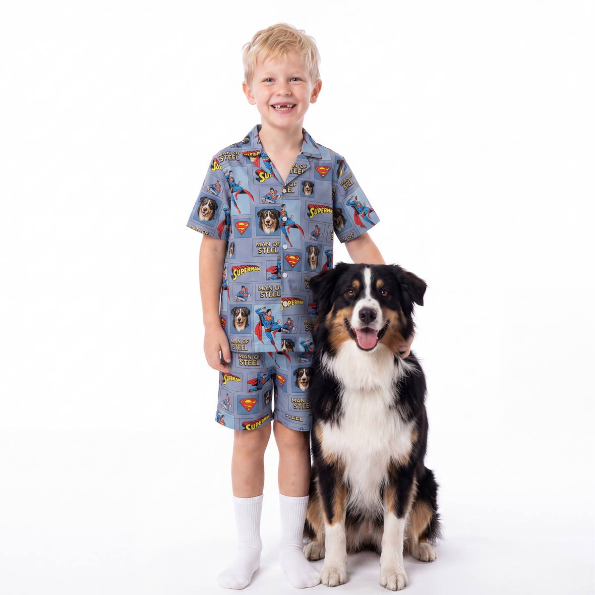 Child wearing a superman pajama set standing next to a dog on a white background