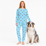 Woman wearing a blue jogger pajama set with dog pattern, sitting next to a dog on a white background