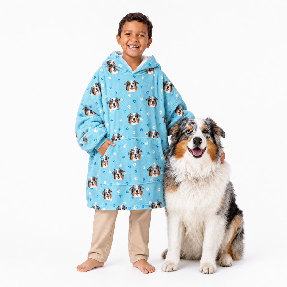 Child wearing a light blue blanket hoodie with dog pattern standing next to a dog on a white background