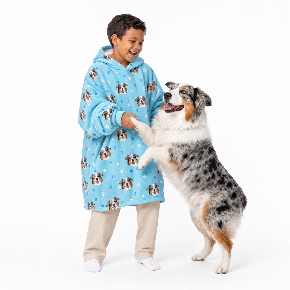 Child wearing a light blue blanket hoodie with dog patterns, standing next to a dog on a white background