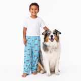 Child wearing Light Blue pajama pants with dog pattern and a dog sitting next to them on a white background